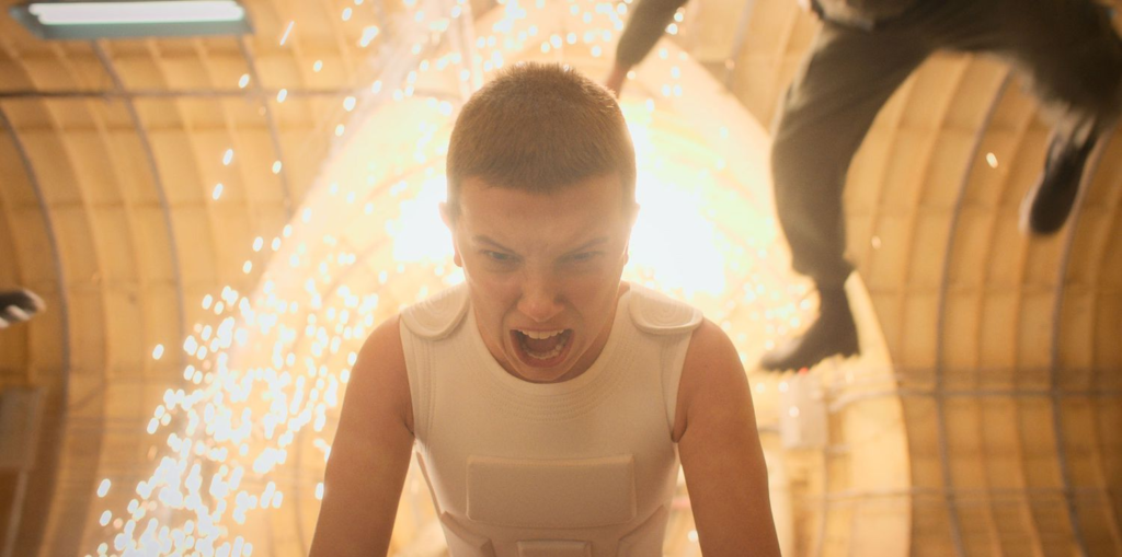 Millie Bobbie Brown as Eleven, shouting angrily as sparks fly behind her.
