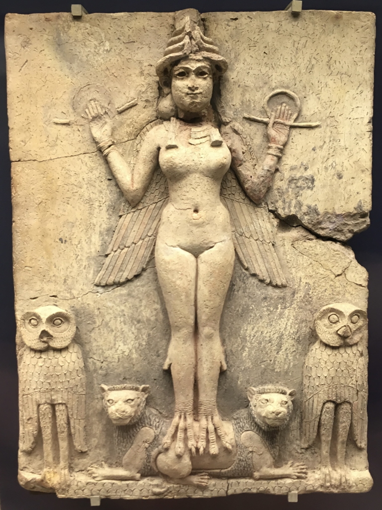 Bas relief of an image of a winged goddess with bird feet who is standing on the backs of two lions, flanked by two owls.