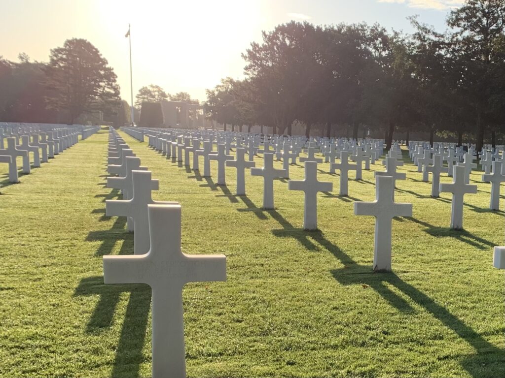 Rows of white marble grave markers in the shape of crosses with the sun rising near the far horizon.